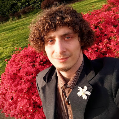 Picture of a dapper man in a dark suit with a flower that took way too long to put onto the breast (the flower is real, and his curls are natural).